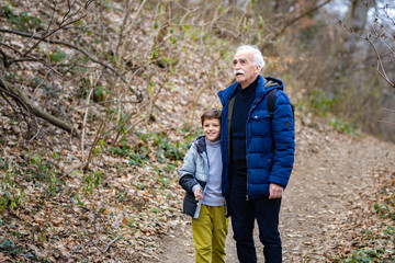 Little boy smiling at the camera while taking a walk with his grandfather in the forest