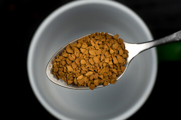 Close-up of a teaspoon with granulated instant coffee over a mug, macro. Top view