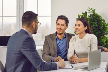 Young family couple meeting with real estate agent or loan broker. Happy, smiling man and woman...