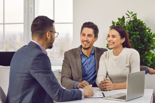 Young family couple meeting with real estate agent or loan broker. Happy, smiling man and woman sitting at office desk with realtor, business advisor or loan manager