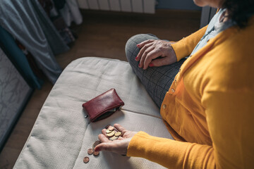 Rear aerial image of an older woman sitting up in bed taking coin money out of her purse and placing it on the bed for counting.