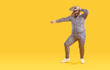 Funny overweight man having fun in rubber mask of dinosaur head isolated on orange background....
