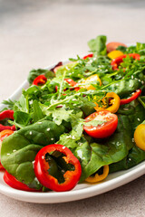 Salad of fresh farm vegetables in an oval dish on a pink background, sitya lettuce and chard, tomatoes and colorful bell peppers, arugula and sesame seeds
