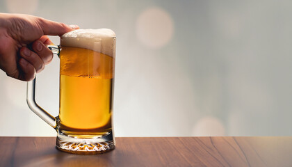 One hand is holding a beer glass on a table. Neutral background. Space for text.