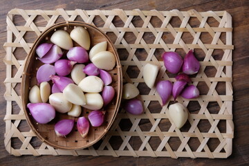 Peeled shallots and peeled garlic in a woven bamboo basket on a wooden table. herbs. spices. spice. 