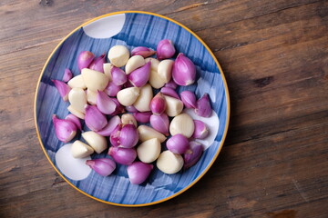 peeled shallots and peeled garlic in a ceramic plate with Asian motifs on a wooden table. herbs. bawang merah bawang putih kupas. 