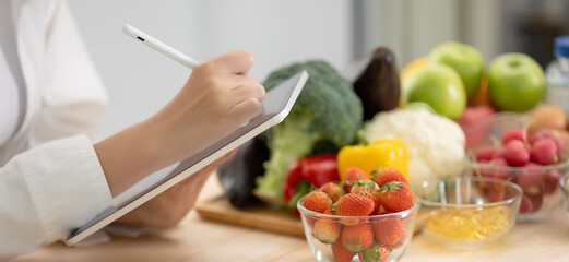 Panoramic of hand professional nutrition healthful surrounded by a variety of fresh fruits and vegetables working on digital tablet. Concept of right nutrition, diet and healthcare. - obrazy, fototapety, plakaty