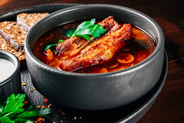 Solyanka soup with meat, sausage, vegetables, olives and lemon in bowl on wooden table background