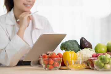 Close up hand of professional nutrition healthful surrounded by a variety of fresh fruits and vegetables working on digital tablet. Concept of right nutrition, diet and healthcare.