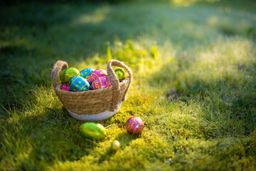 Easter eggs in basket in grass. Colorful decorated easter eggs in wicker basket. Traditional egg hunt for spring holidays. Morning magical light.