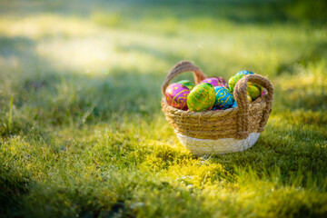 Easter eggs in basket in grass. Colorful decorated easter eggs in wicker basket. Traditional egg hunt for spring holidays. Morning magical light.