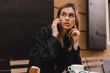 Doubtful young adult woman talking on cell phone making call looking away thinking of solution sitting in cafe, considering offer, making decision or feeling doubt.