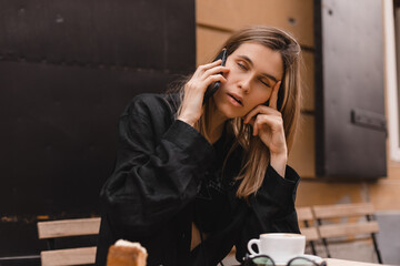 Portrait of beautiful young woman bored talking sitting in cafe with coffee and piece of cake. Girl...