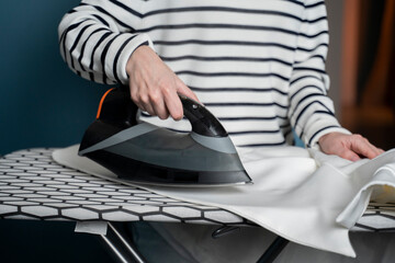 Woman irons clothes on an ironing board in the laundry room at home close-up. 