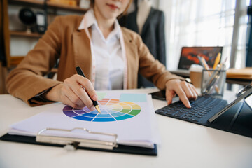 Fashion designer woman talking smart phone and using laptop with digital tablet computer in modern studio in morning light.