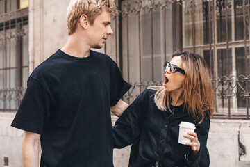 Couple walking outdoor, they hug. Woman look shocked with open mouth on her man and hold coffee take away. Unfaithful relationship concept. Wife suspects her husband is disloyal. Furious woman. - obrazy, fototapety, plakaty