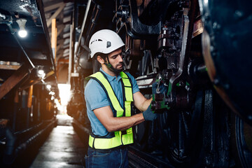Obraz na płótnie Canvas Male engineer maintenance locomotive engine wearing safety uniform, helmet and gloves work in locomotive repair garage. 