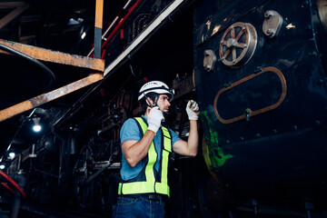 Male engineer maintenance locomotive engine wearing safety uniform, helmet and gloves work in locomotive repair garage. 