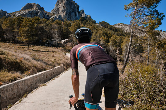 Man cyclist on a gravel bike riding on the road in the hills with a view of the mountains.Man cyclist wearing cycling kit and helmet.Gravel bike with cycling bag.Sport motivation.Alicante region,Spain