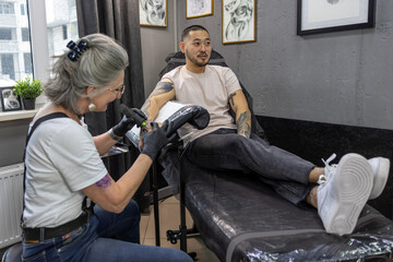 Fototapeta na wymiar Tattoo master wotking on a tattoo for the male client