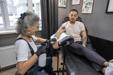 Fototapeta na wymiar Gray-haired tattoo owner working with the client