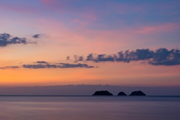 Fototapeta na wymiar Calm waters of the sea with silhouettes of islands and mountains under the purple sunset sky
