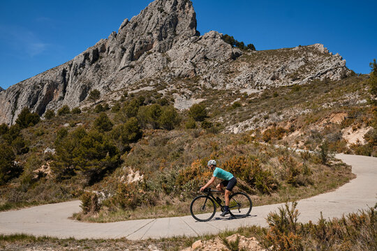 A female cyclist is training on a mountain pass on a gravel bike.Woman riding on bicycle in the mountains.Cyclist wearing a cycling kit and helmet.Gravel cycling adventure.Guadalest Reservoir,Spain.