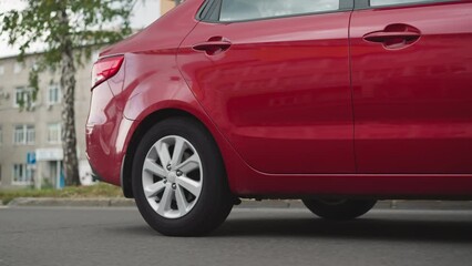 Red car sedan drives on empty street passing old buildings on sunny summer day. Elegant classy automobile moves on asphalt road in town closeup