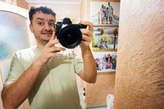 Funny man photographer making selfie with camera in mirror at home.