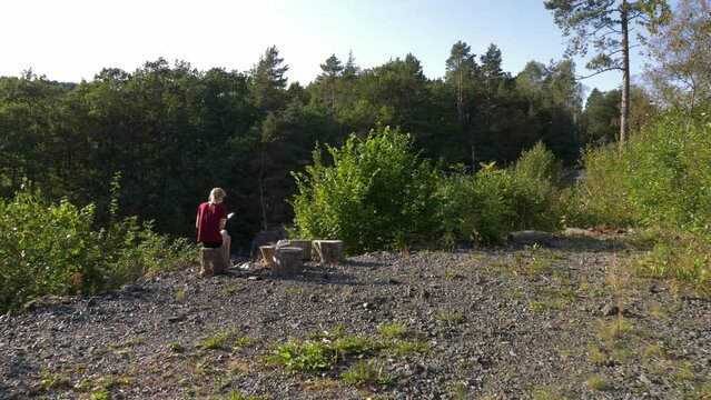 Slow motion camera view of woman camping in the Norway. Young female reads book next to the rock waterfall. Evening relaxation. Nature.