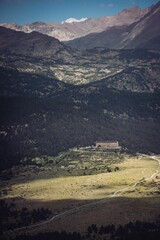 Vertical shot of a lonely building in front of high mountains covered in forests, Pyrenees, France