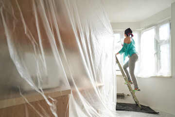 Woman stands on the stairs and paints the wall with a roller