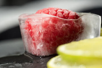 alcuni cubetti di ghiaccio con al loro interno laponi e mirtilli, con fette di lime, un piano in ardesia con al di sopra dei cubetti di ghiaccio con frutta