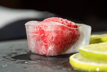 alcuni cubetti di ghiaccio con al loro interno laponi e mirtilli, con fette di lime, un piano in ardesia con al di sopra dei cubetti di ghiaccio con frutta