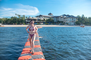 A sexy woman in a sexy plaid bikini standing on on floating pontoon near a luxurious resort....