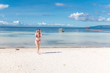 A beautiful short haired asian woman in a plaid bikini walking away from the shoreline of a white sand beach. Basking in the hot tropical sun.