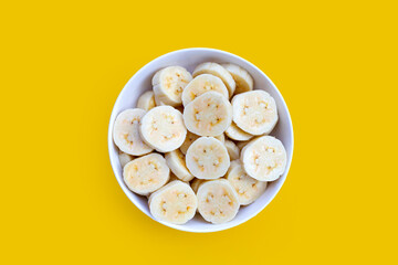 Banana slices in bowl on yellow background.