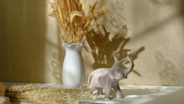 Vase with dried flowers and moving shadows on beige background casting shadows . Ivory elephant. Minimal modern interior decoration concept. Autumn wabi sabi style aesthetics