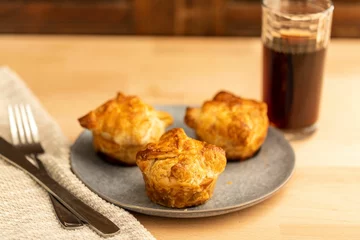  High-angle view of three kouign-amanns in the gray plate and a glass of drink over the wooden table © Cameron Stuart Fowles/Wirestock Creators