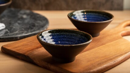 Two brown bowls with blue design placed over the wooden cutting board