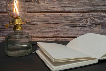 Closeup of a burning old antique hurricane oil lamp with open book on wooden table