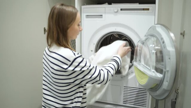 Smiling brunette, a decent housewife, stands in the laundry room and loads the washing machine with dirty clothes. 