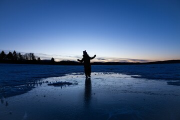 Fototapeta premium Silhouette of a young kid standing on the ice in the mountains in winter