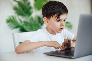 a boy sitting at a table playing at a laptop in the room