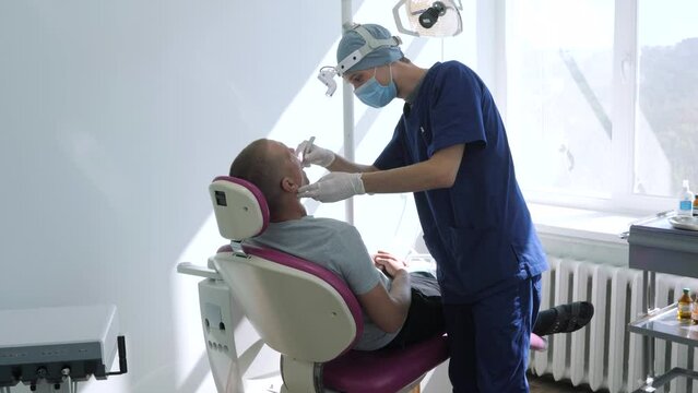 Dentist in a protective face mask when working with a patient. Modern dentist cabinet. Teeth care, dental health.
