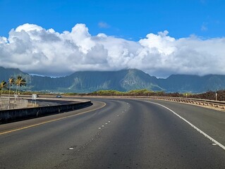 Scene of the road between mountains and palm trees with heavy white clouds in Oahu, Hawaii