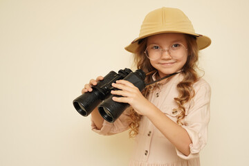 Traveler child. Child discoverer. Young researcher. Little girl in a safari hat with binoculars in her hands. Concept: search for adventure and treasure. Cute happy girl in safari clothes