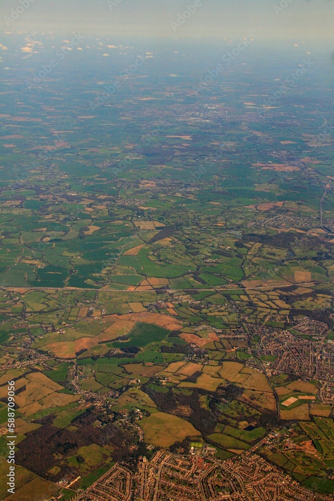 Sticker Vertical aerial shot of green fields, buildings and roads during daytime from a plane