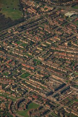 Vertical aerial shot of green fields, buildings and roads during daytime from a plane