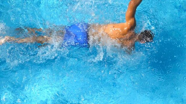 Close up of unrecognizable sporty guy floating across pool with clear blue water. Young man swimming and enjoying recreation on resort in sunny day. Concept of travel or holiday. Slow motion Top view